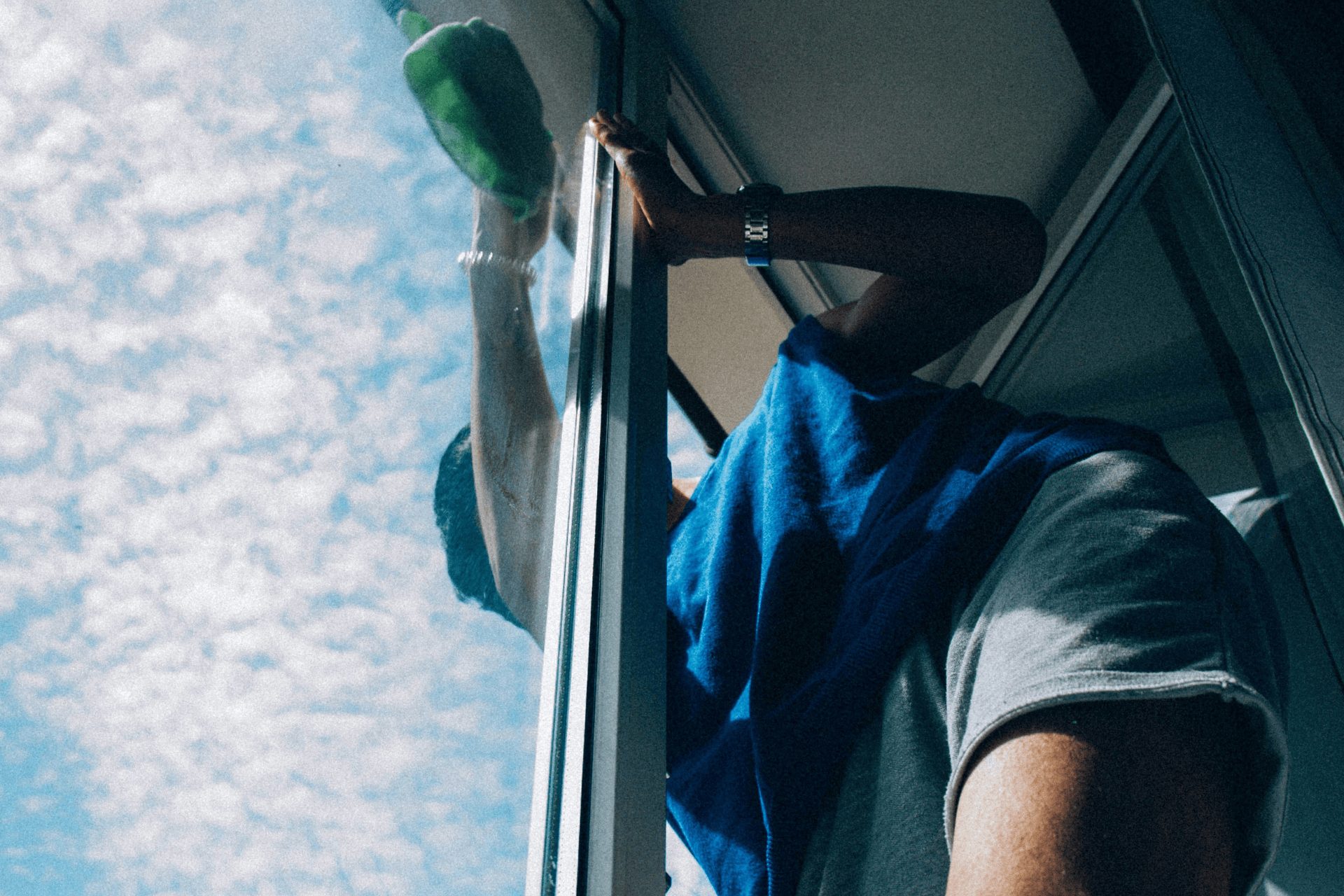 A woman leaning out of her window to clean her glass instead of hiring a professional window cleaner in Tunbridge Wells